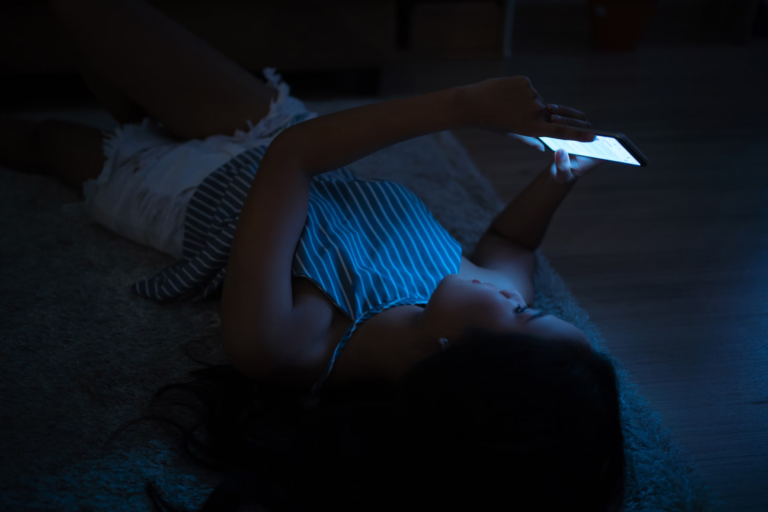 Woman scrolling on phone, on bed, at night